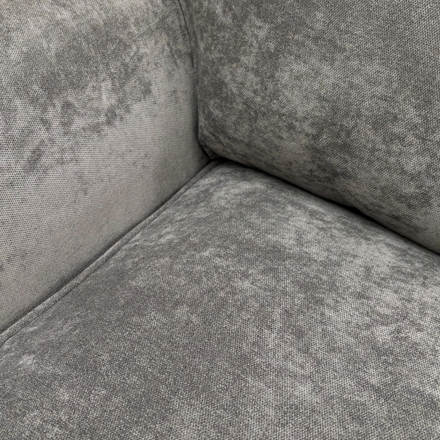 A close-up shot focusing on the texture of the grey fabric and the detail of the stitching on the cushions and arms.