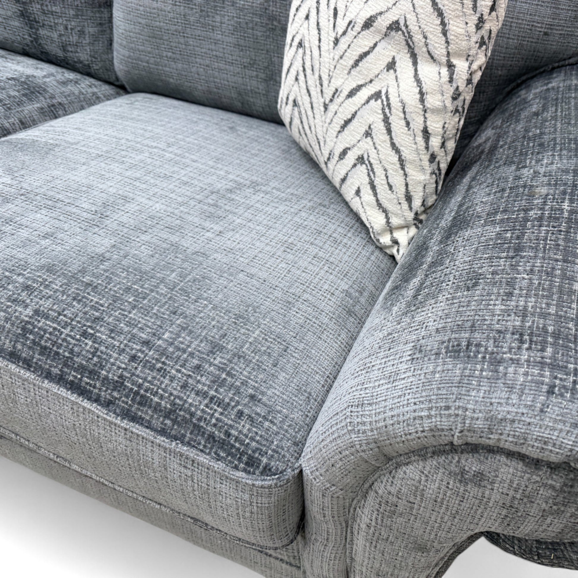 Close-up texture detail of the bluish-grey woven fabric on the 'Clara' sofa, showing the material's intricate weave and subtle color.