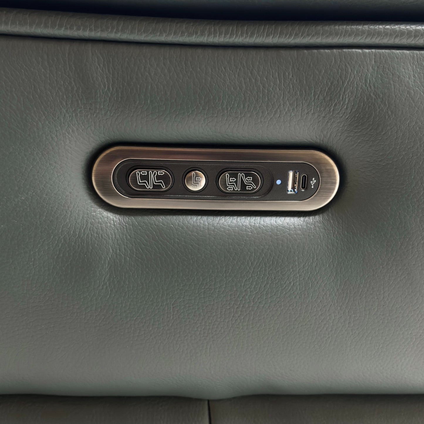 A close-up on the end armrest, showcasing the control panel with buttons for the power recline, headrest, and the integrated USB charging port.