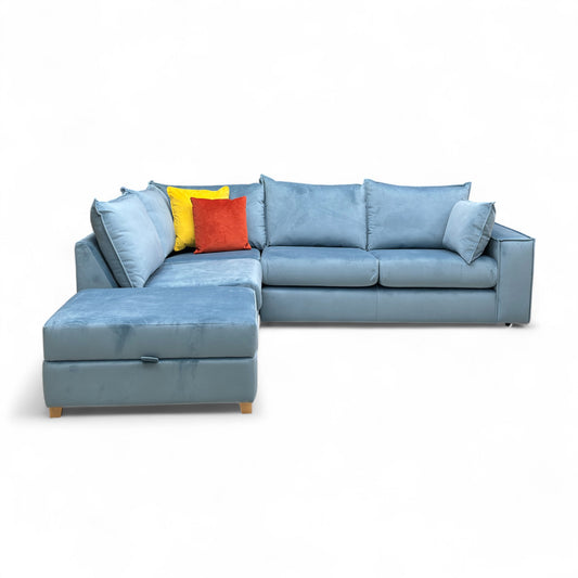Full front-angled view of the L-shaped corner sofa in light blue/sky velvet, showing the right-hand facing arm and the separate footstool.
