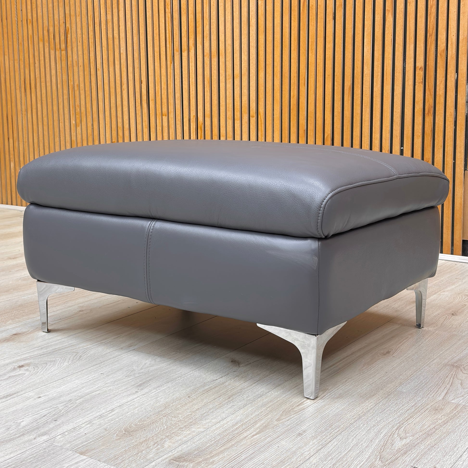 Lifestyle view for the Vino leather footstool, highlighting the 100% genuine Lavender Grey leather and its versatile use as a seat or leg rest.