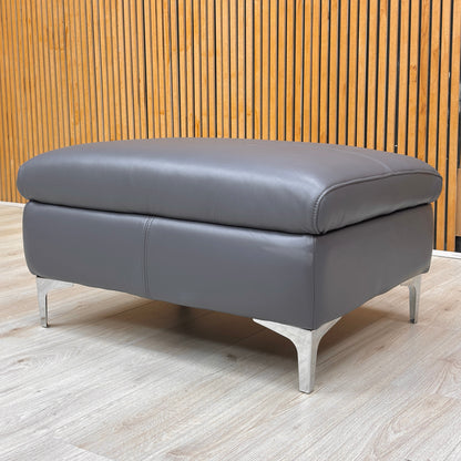 Lifestyle view for the Vino leather footstool, highlighting the 100% genuine Lavender Grey leather and its versatile use as a seat or leg rest.