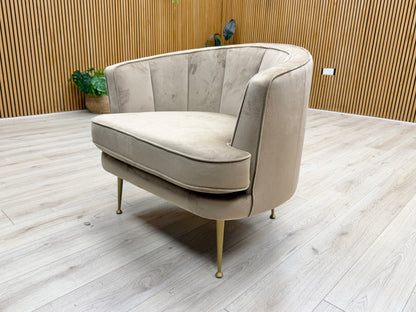 Stylized lifestyle shot of the ‘Enchanted’ latte velvet chair, highlighting its elegant curved armrests and boutique design.