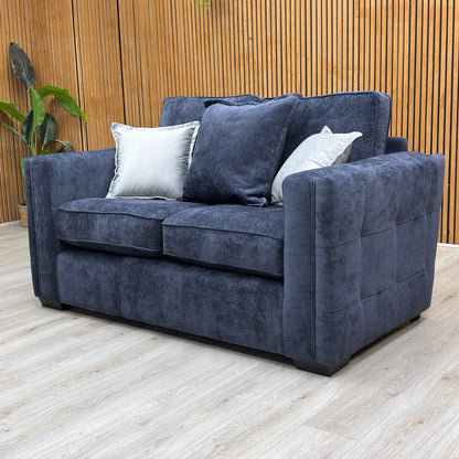 Lifestyle view of the Chelsea denim blue sofa in a cozy, modern living room setting with soft ambient lighting.