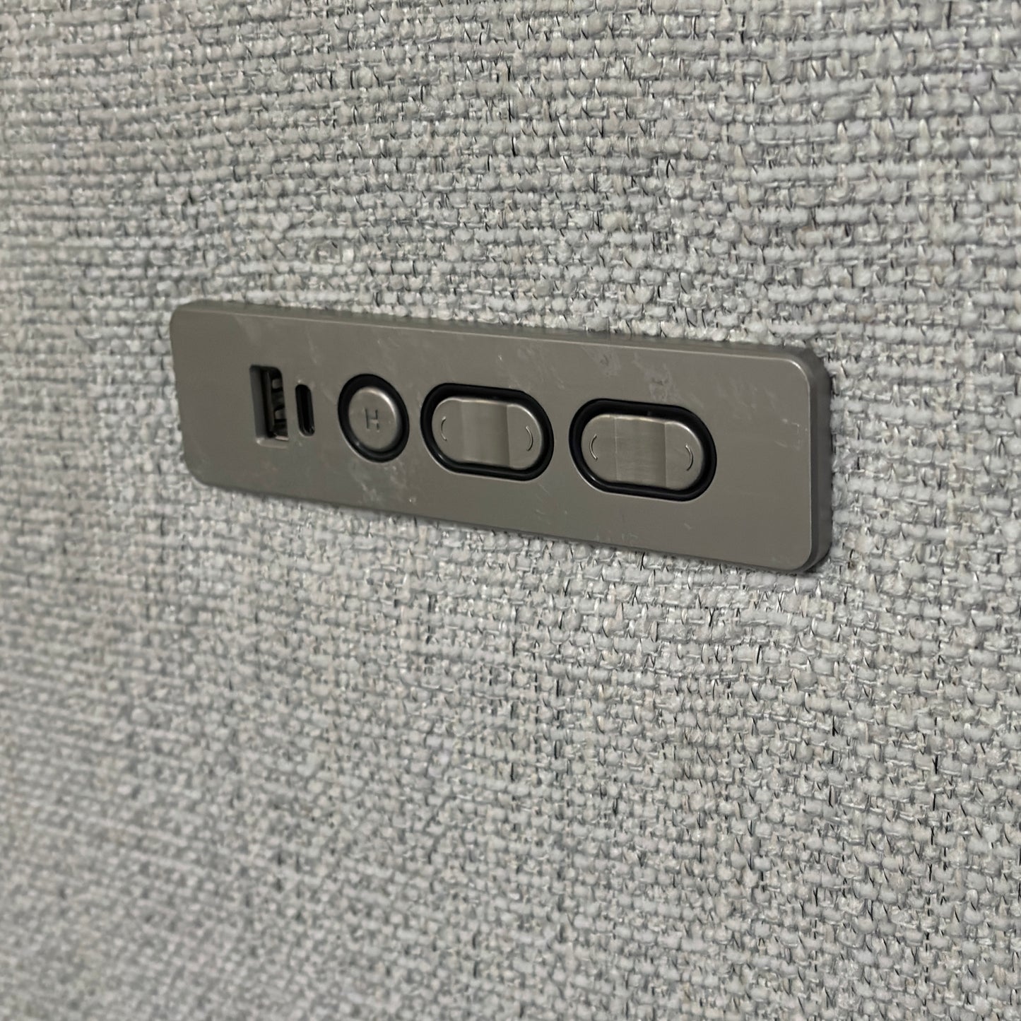 Close-up of the grey metal power control panel for a reclining sofa or chair, embedded into textured fabric.