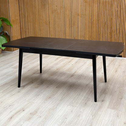 Magda black solid oak extending dining table extended, against a slatted wooden wall on a light oak floor