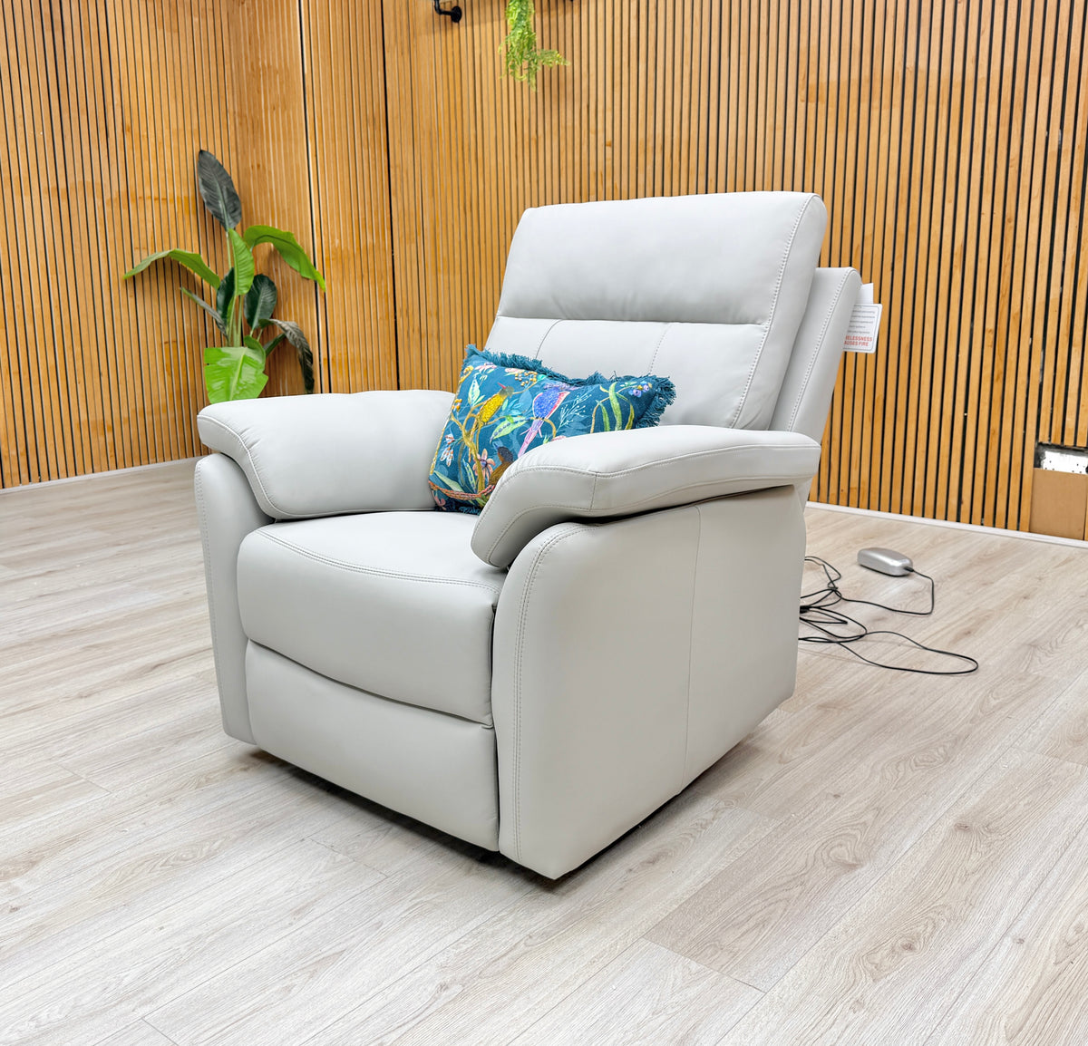 The power recliner armchair from the Sally light grey leather set against a slatted wooden wall, lead visible