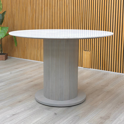 Lifestyle view of the Aimar table, showcasing the 115cm circular surface and the ample legroom provided by the central base.