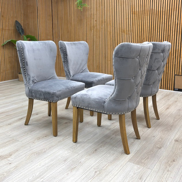 lifestyle view of a Chennai dining chair, showcasing the ergonomic curved backrest and the contrast between the silver studs and deep grey velvet.