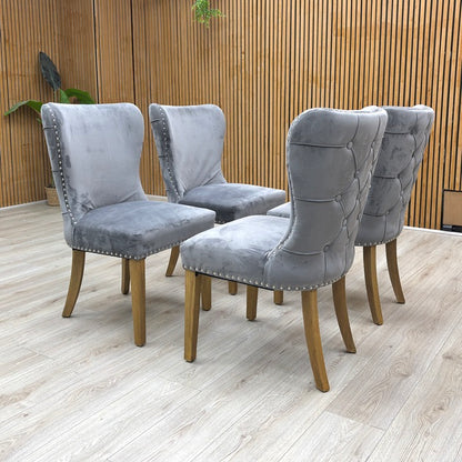 lifestyle view of a Chennai dining chair, showcasing the ergonomic curved backrest and the contrast between the silver studs and deep grey velvet.