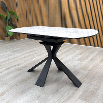 Lifestyle view of the Crete dining table in its compact round form, showcasing the durable textured stone finish and the architectural geometric leg design.