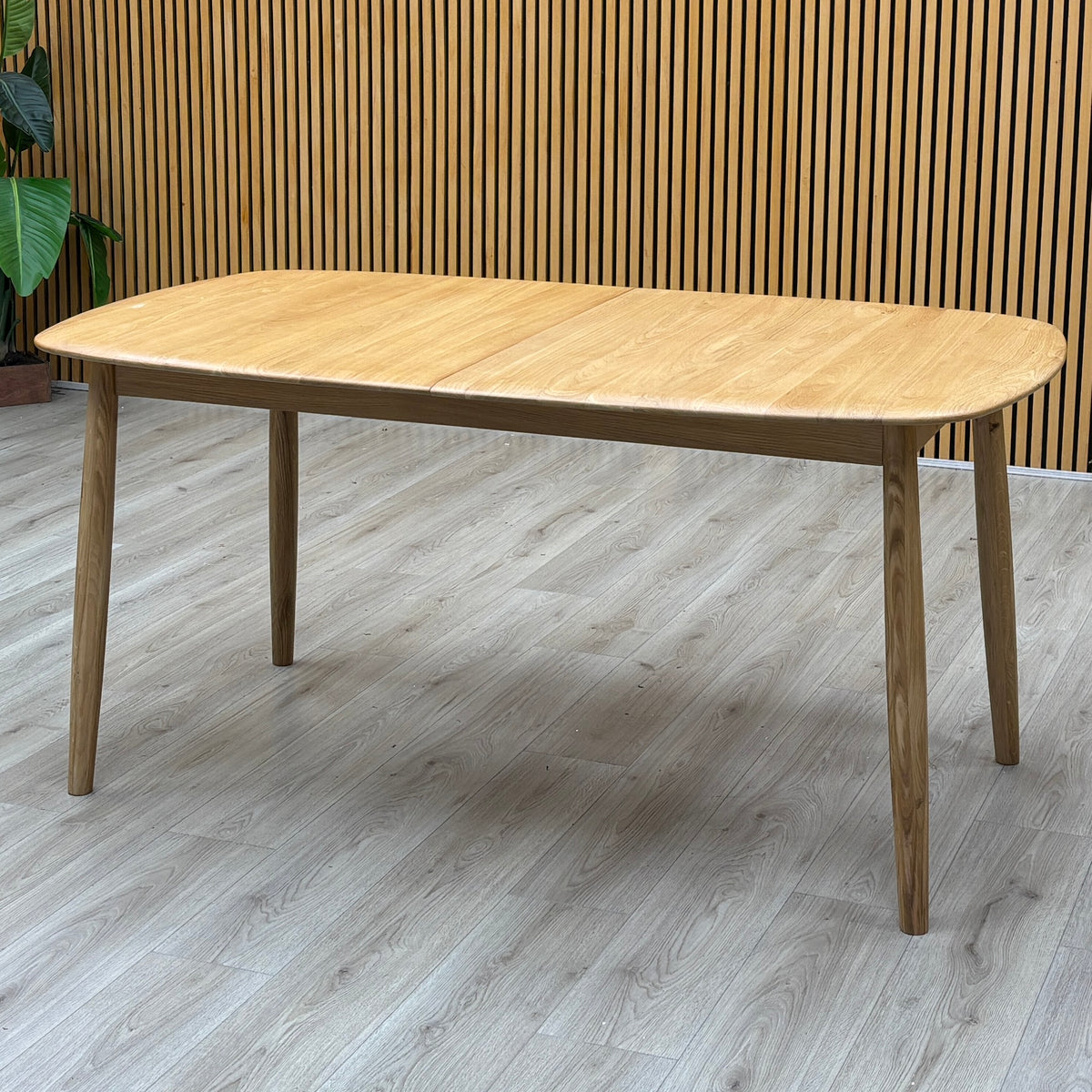 Stockholm light oak extending dining table against a slatted wooden wall on a grey wood-effect floor