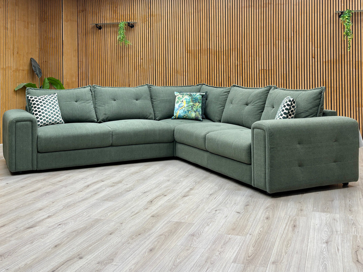 Goliath moss green fabric large corner sofa against a slatted wooden wall on a pale wood floor
