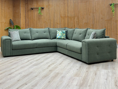 Goliath moss green fabric large corner sofa against a slatted wooden wall on a pale wood floor