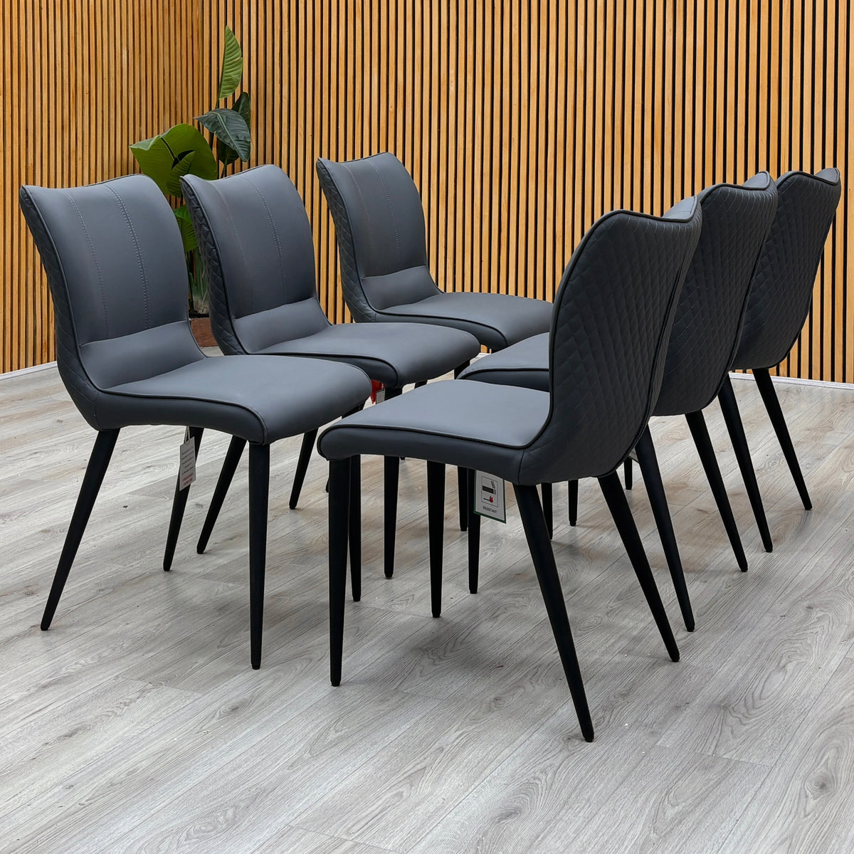 Clio grey faux leather dining chairs, set of six, against a slatted wooden wall on a light floor