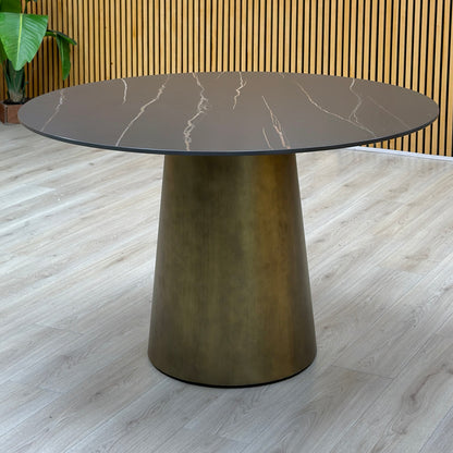 Osiris golden black sintered stone round dining table on a bronze cone base against a slatted wood wall