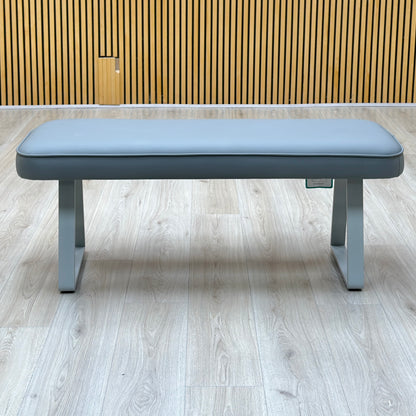 Front view of the Fumo light grey faux leather dining bench against a slatted wooden wall on a light oak floor