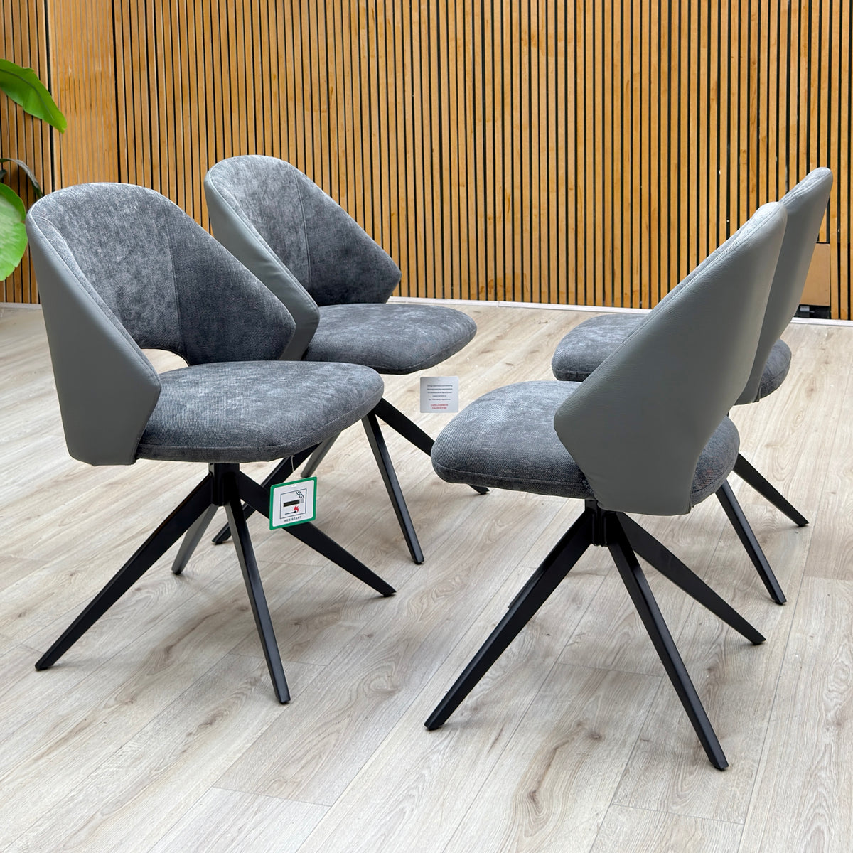 Raul anthracite grey faux leather swivel dining arm chairs, set of four, against a slatted wooden wall