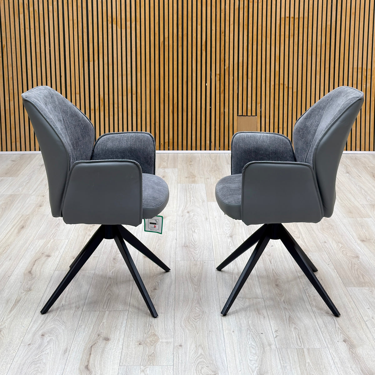 Julio anthracite grey faux leather pair of swivel dining chairs facing each other against a slatted wooden wall