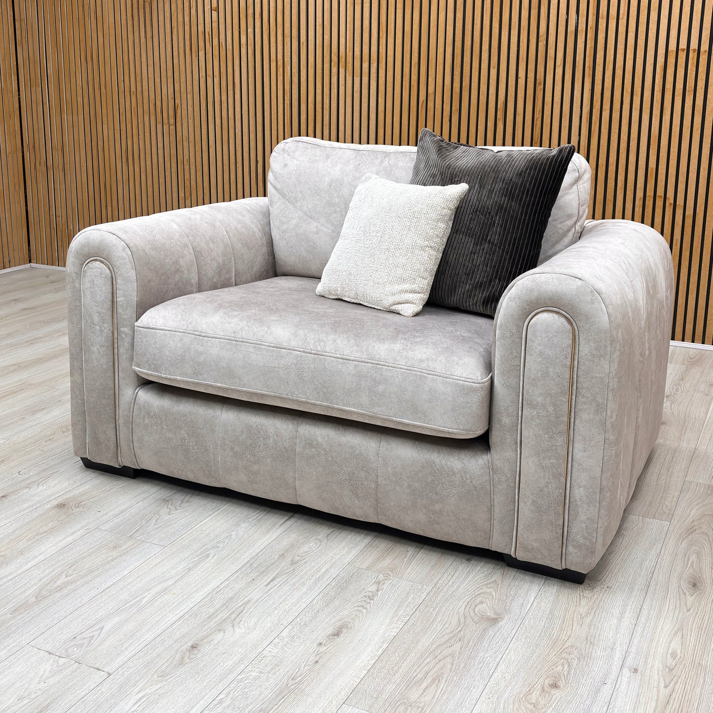 Side view of the Amara snuggle chair, upholstered in a premium stone grey fabric and featuring a wide, deeply cushioned seat and plush over-padded armrests.