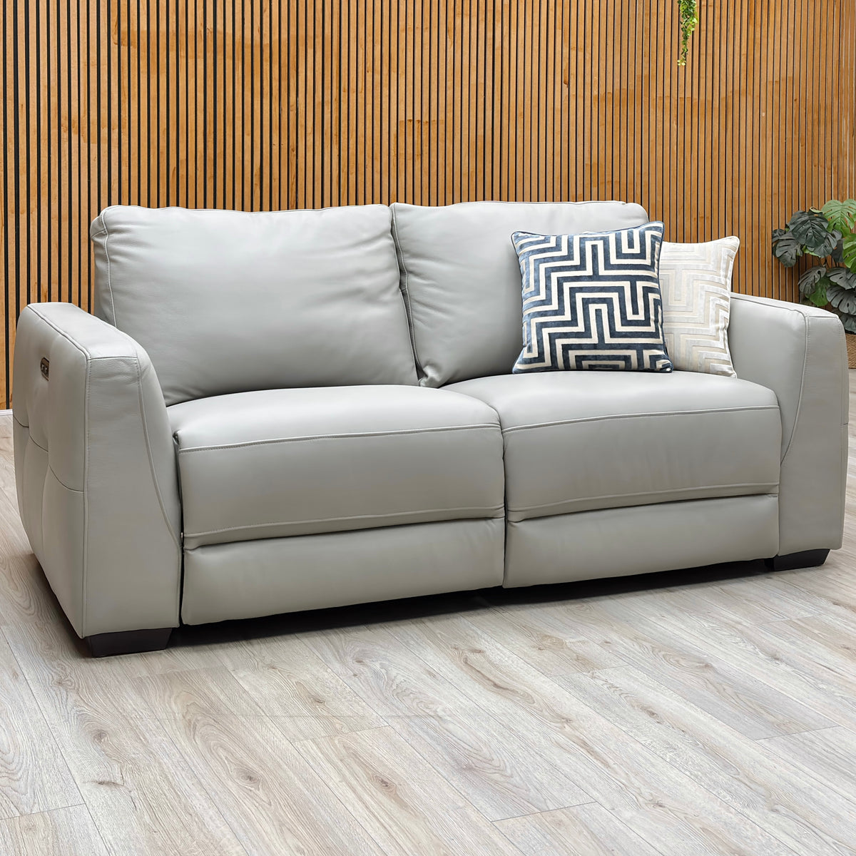 Dinky light grey leather 3 seater power recliner sofa against a slatted wooden wall on a light oak floor