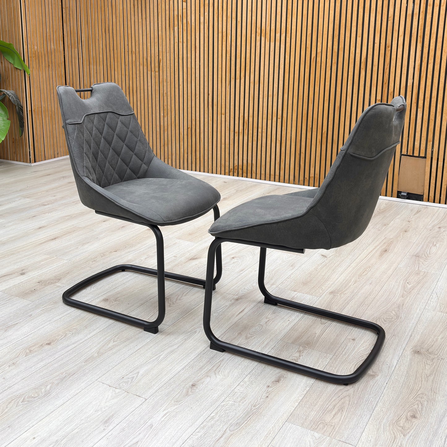 Lifestyle view of the ‘Warrior’ cantilever chair, emphasizing the comfortable deeply padded seat cushion and the bold contrast between the charcoal grey upholstery and dark frame.