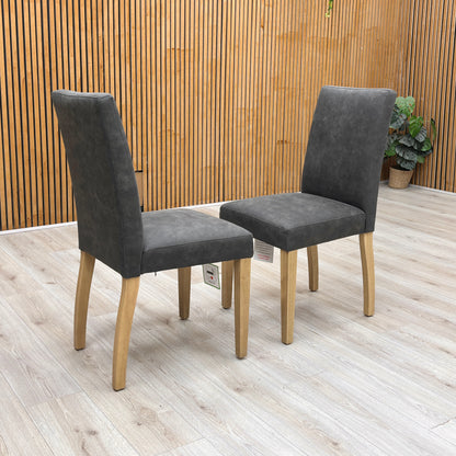Lifestyle view of the ‘Augusta’ dining chair, emphasizing the comfortable deeply padded seat cushion and the elegant monochromatic look of the grey upholstery with dark legs.