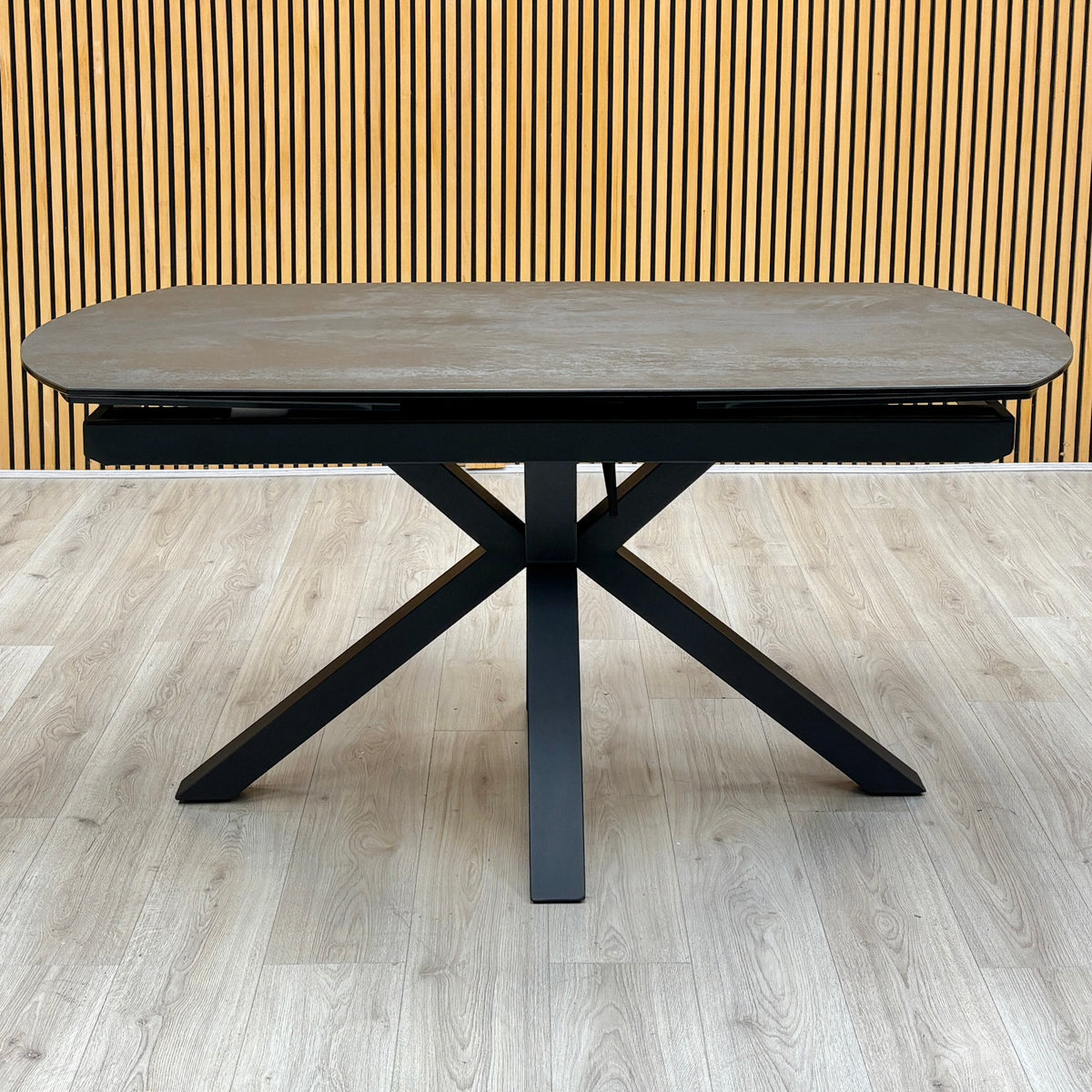 Front view of the Raul titanium grey ceramic 160cm dining table on a black spider base, on a light oak floor