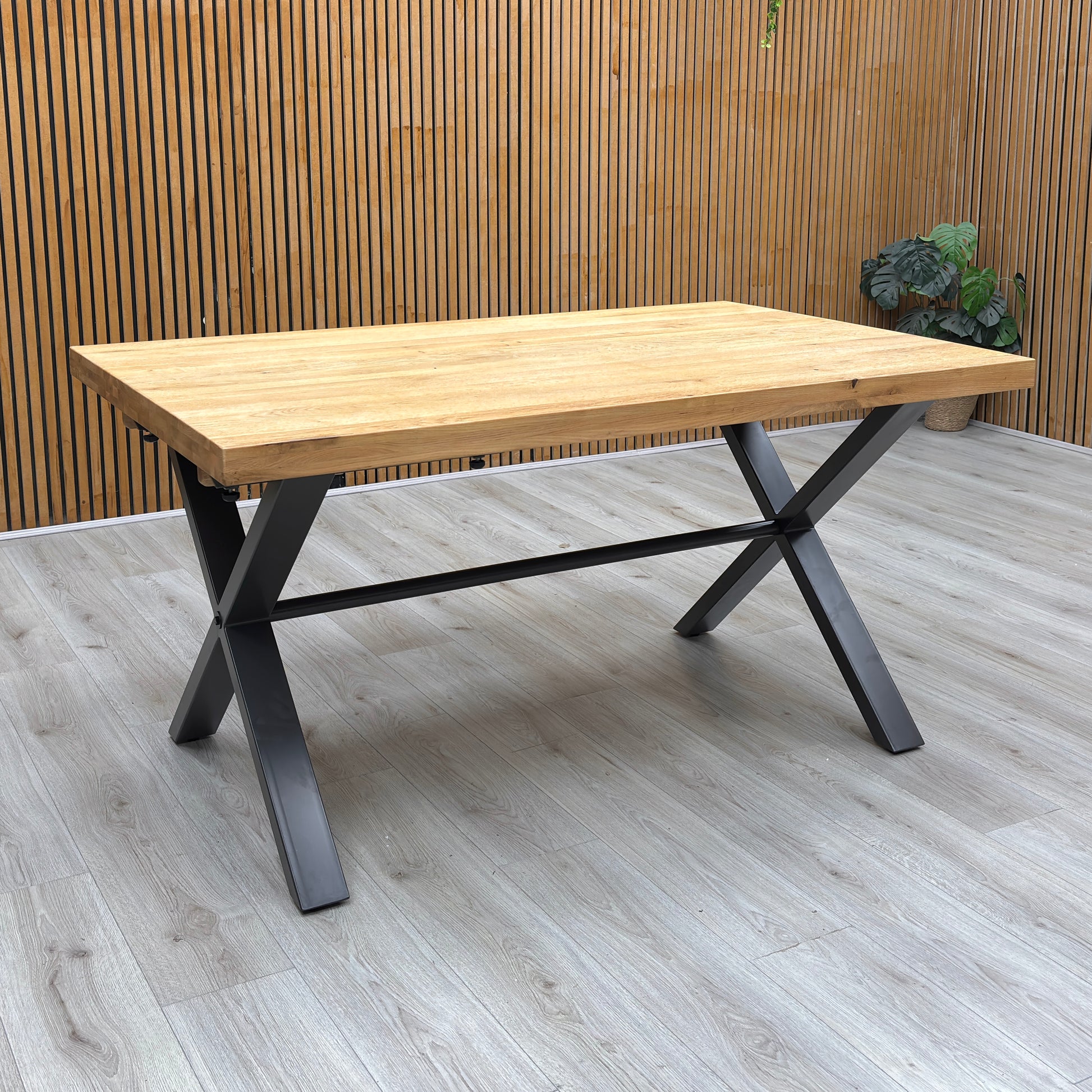 Lifestye view of the ‘Earth’ dining table, emphasizing the unique natural wood grain patterns, organic knots, and the striking X-shaped metal base structure.