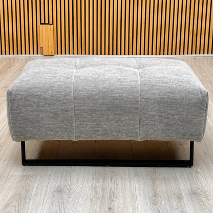 Shelby dove grey fabric footstool photographed against a slatted wooden wall on a light oak floor