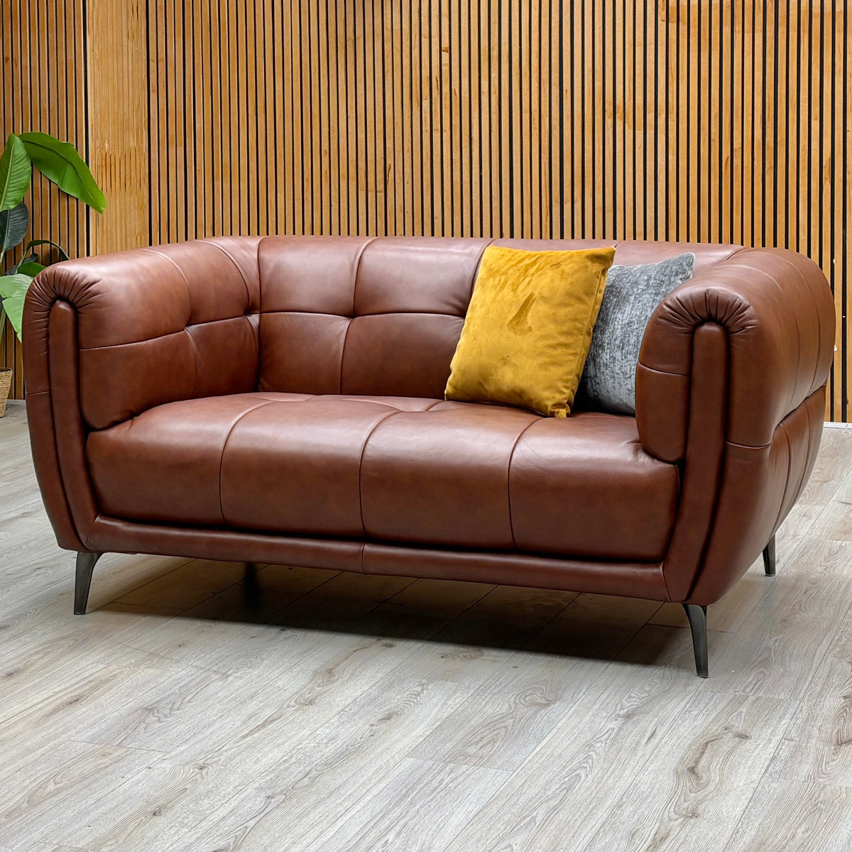 Sienna butterscotch brown leather 2 seater sofa against a slatted wooden wall on a light wood floor