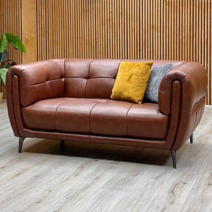 Sienna butterscotch brown leather 2 seater sofa against a slatted wooden wall on a light wood floor