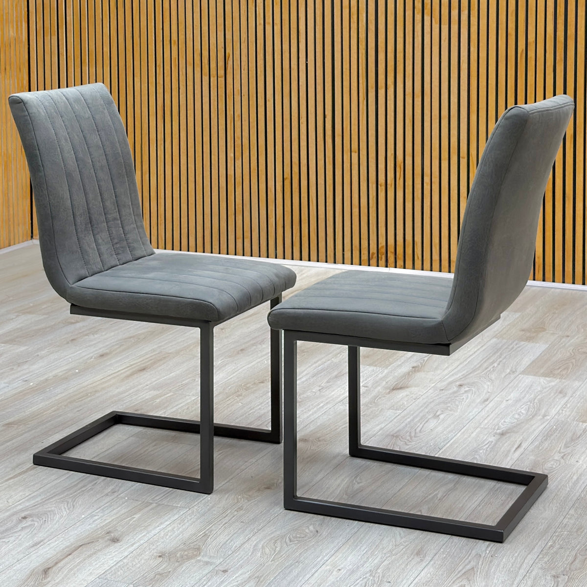 Pair of Moon grey fabric cantilever dining chairs against a slatted wooden wall on a light oak floor