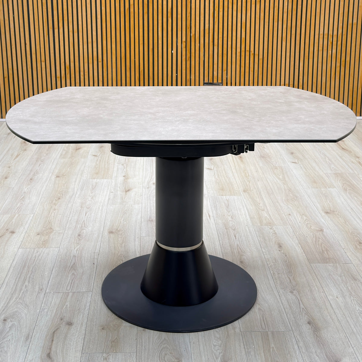 Enterprise grey ceramic top swivel dining table closed, photographed on a light wood floor against a slatted wall