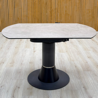 Enterprise grey ceramic top swivel dining table closed, photographed on a light wood floor against a slatted wall