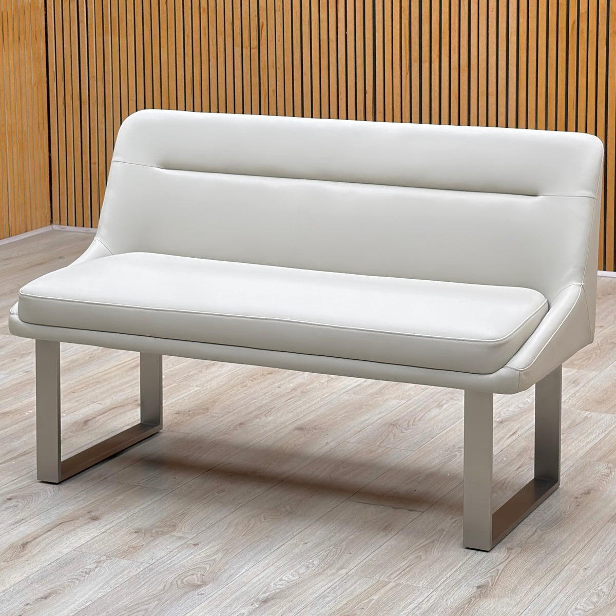 Avorio neutral faux leather high back dining bench against a slatted wooden wall on a light floor