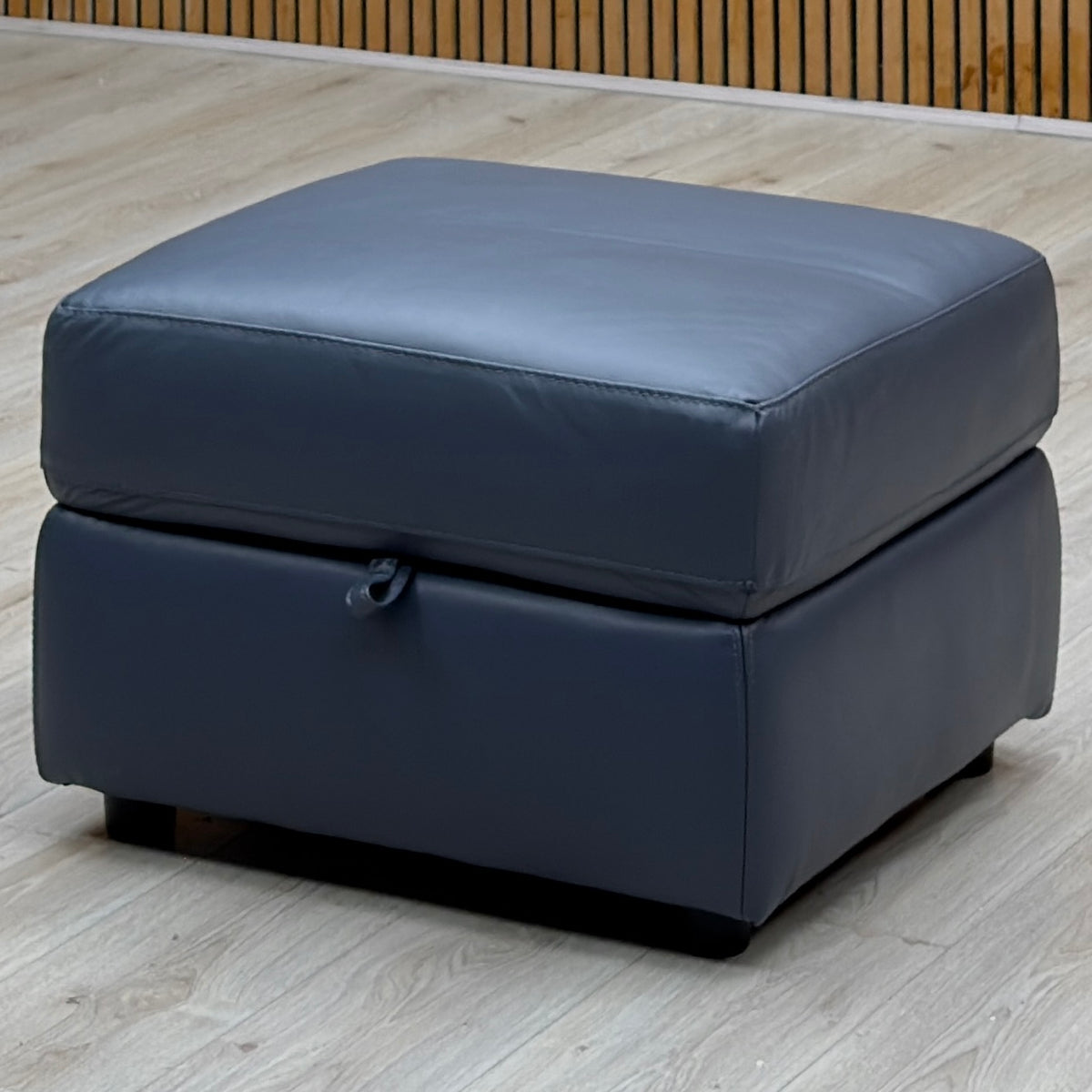 World of Leather Touch ocean blue leather storage footstool on a pale wood floor by a slatted wooden wall