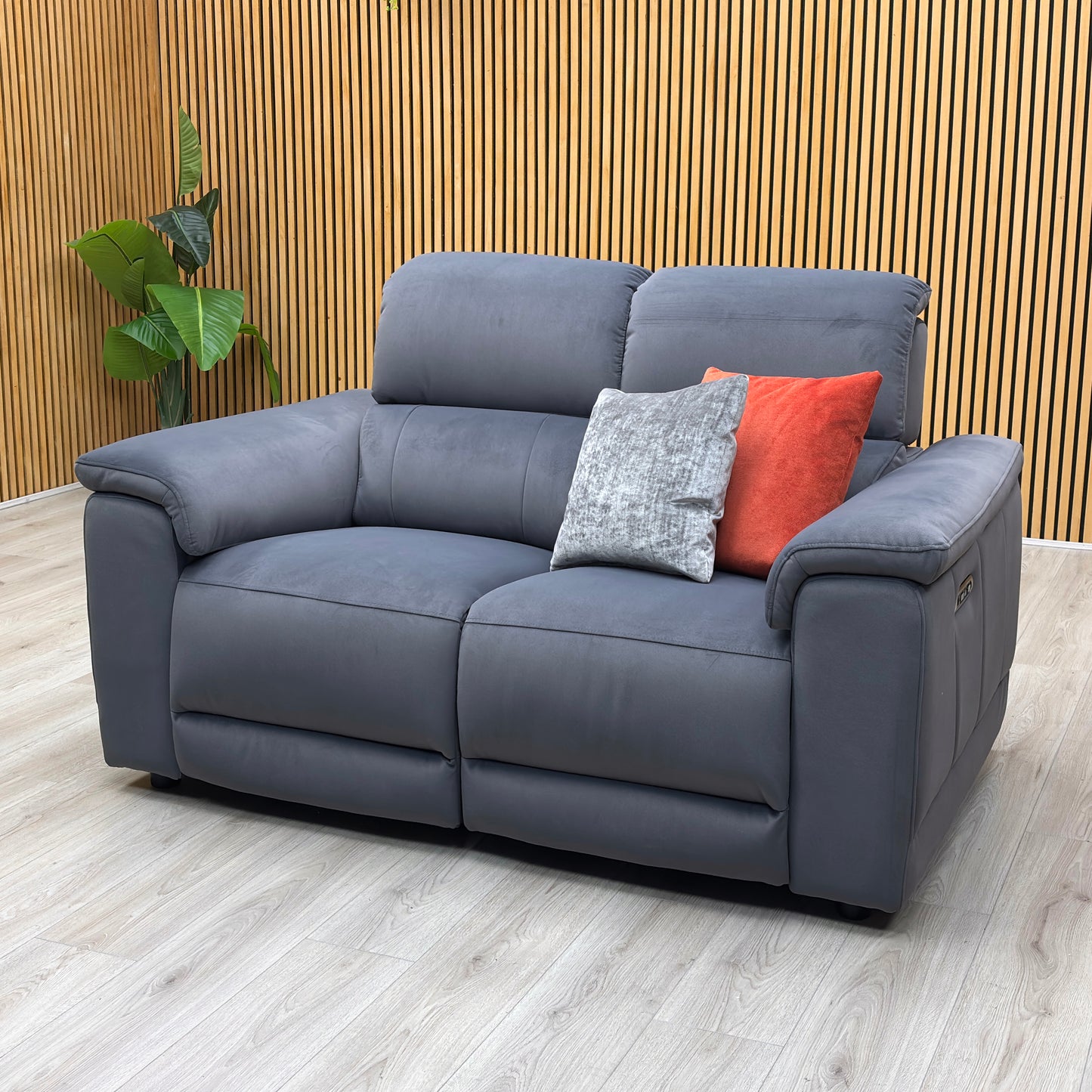 Lifestyle view of three-quarter angled view of the Genius Bella Iron Grey upholstered power reclining love seat, highlighting its deep seat cushions, modern profile, and premium stitching.