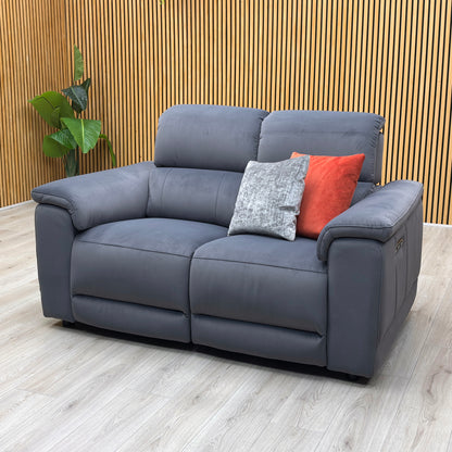 Lifestyle view of three-quarter angled view of the Genius Bella Iron Grey upholstered power reclining love seat, highlighting its deep seat cushions, modern profile, and premium stitching.
