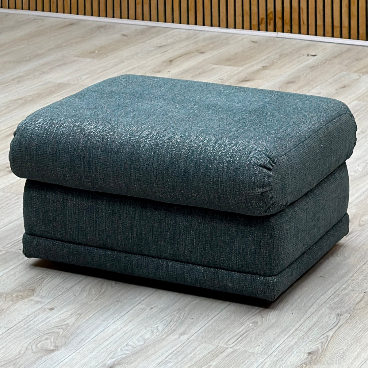 G Plan Malvern teal fabric storage footstool on a light wood floor against a slatted wall