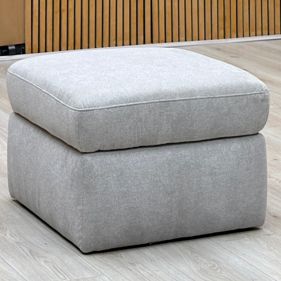 Berlin rosy light grey fabric storage footstool against a slatted wooden wall on a light oak floor