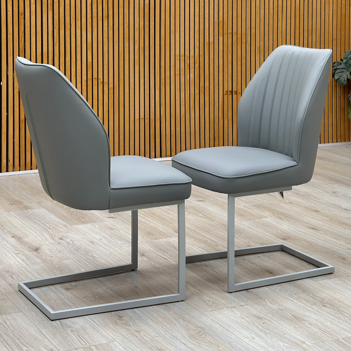 Fumo grey faux leather pair of cantilever dining chairs against a slatted wooden wall on a pale wood floor