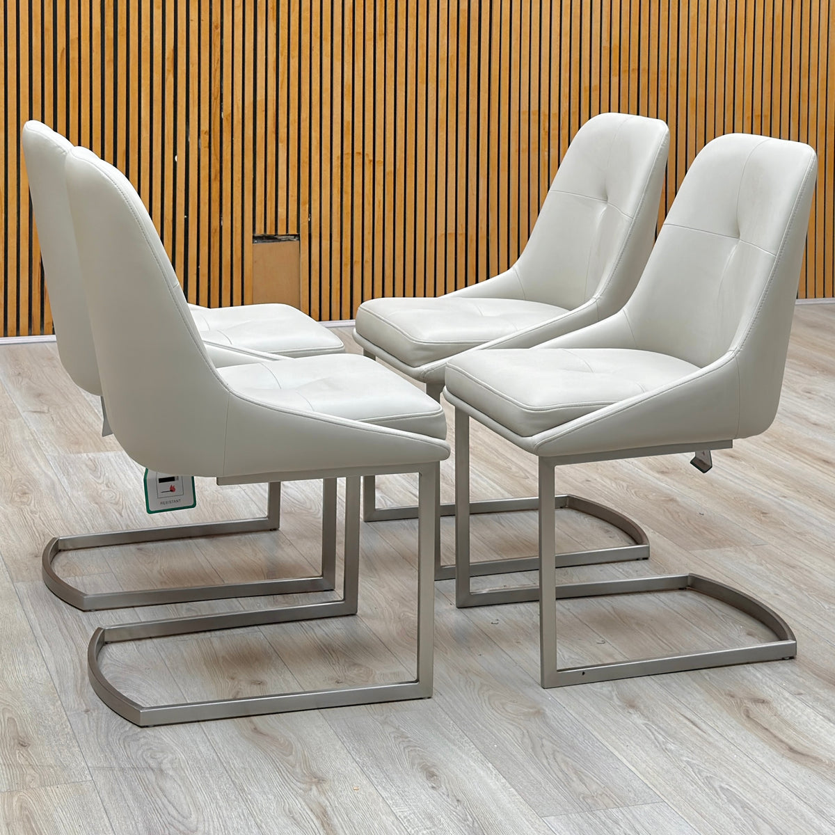 Set of 4 Avorio neutral faux leather cantilever dining chairs against a slatted wooden wall