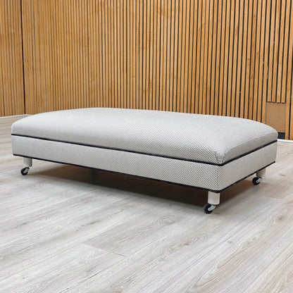 Lifestyle view of the rectangular noir fabric footstool highlighting its low-profile design and soft edges.