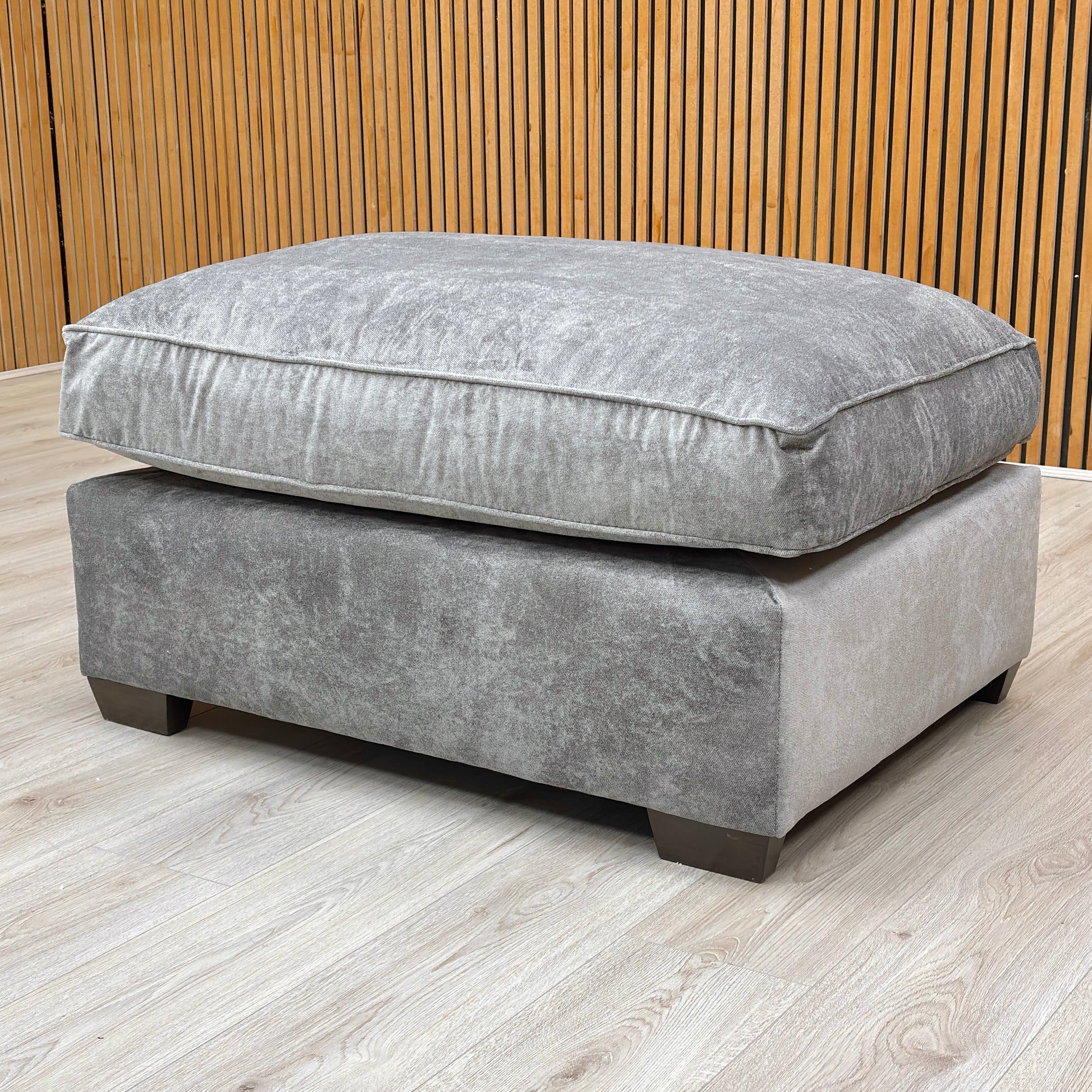 Stylized lifestyle shot of the ‘Rosie’ grey footstool, highlighting the generous seating surface and soft texture.