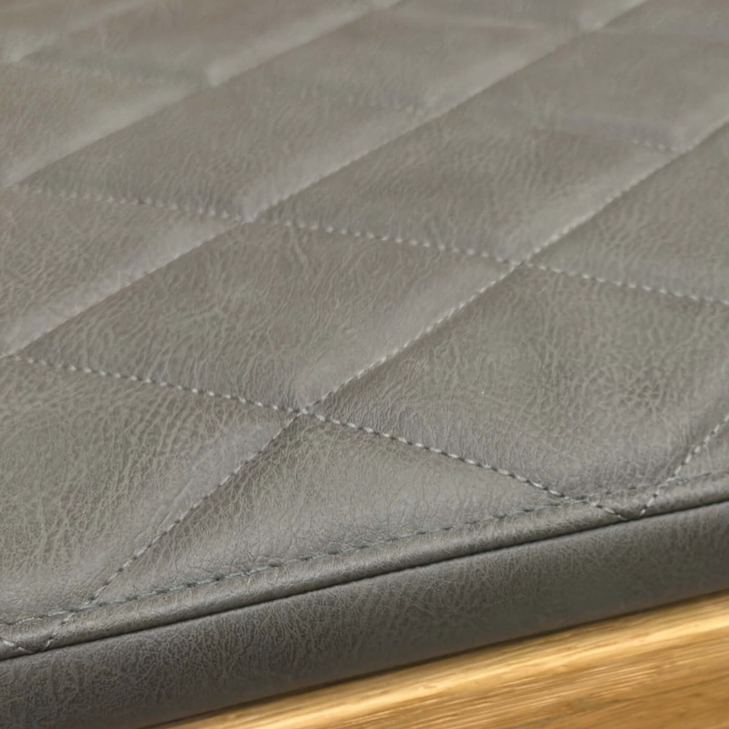 Close-up of a quilted black leather surface with a wooden edge of a bench