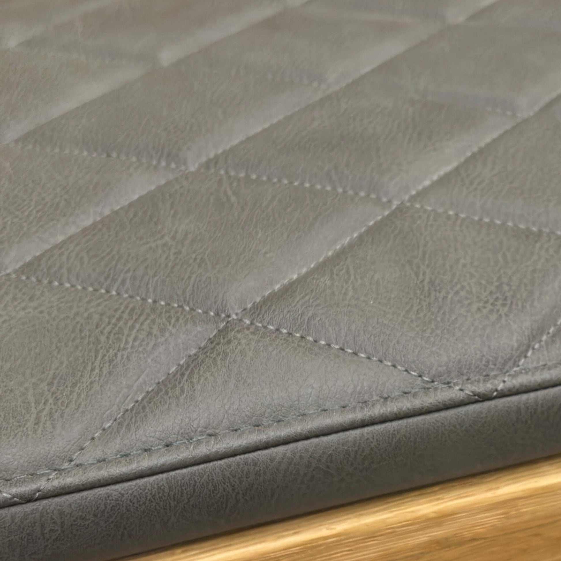 Close-up of a quilted black leather surface with a wooden edge of a bench