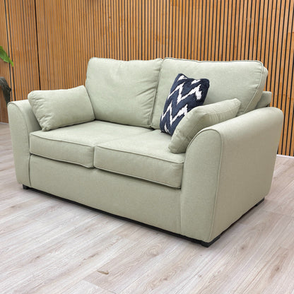 Lifestyle shot of the ‘Julius’ sage green sofa, highlighting its structured formal back and tailored arms.