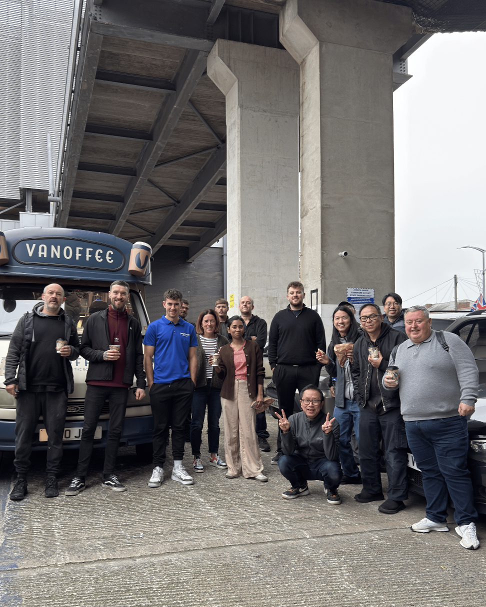 Group of people posing for a photo under a bridge with a Vanoffcc truck in the background.