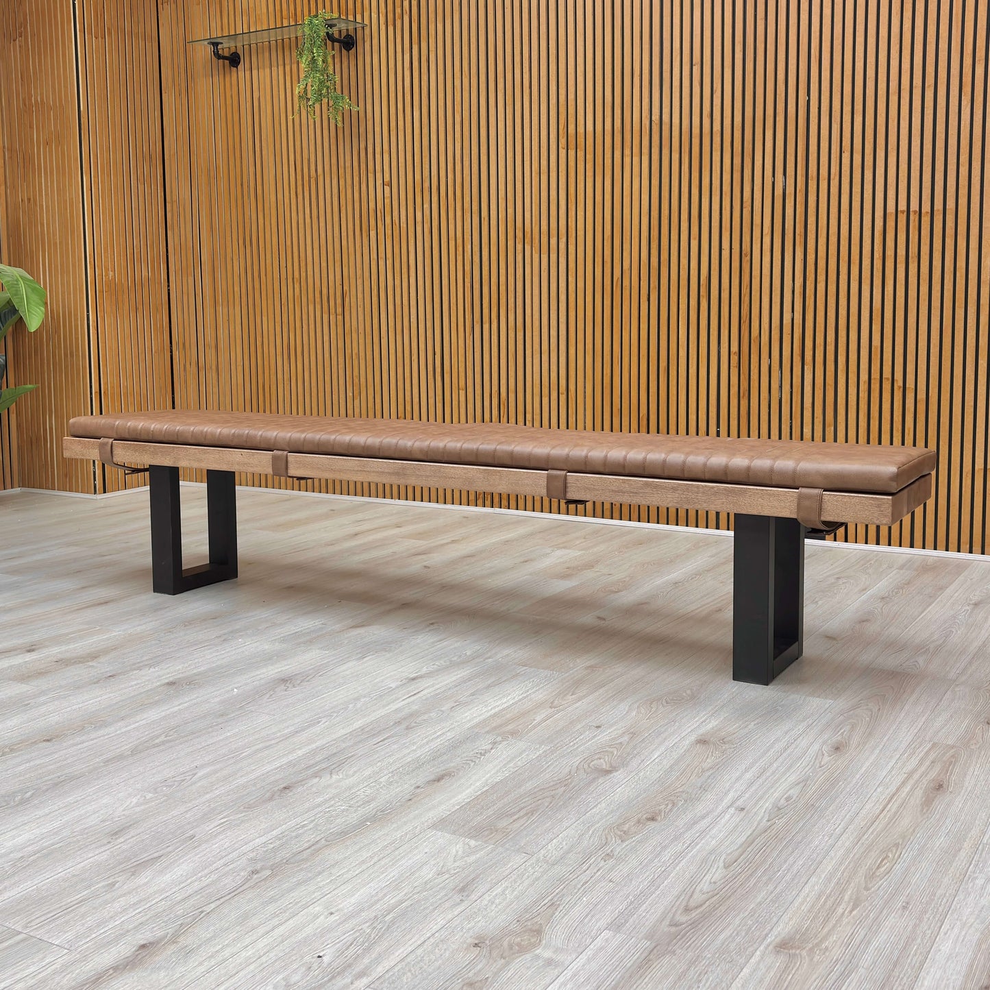 Wooden bench with black legs on a light wooden floor against a wooden wall.
